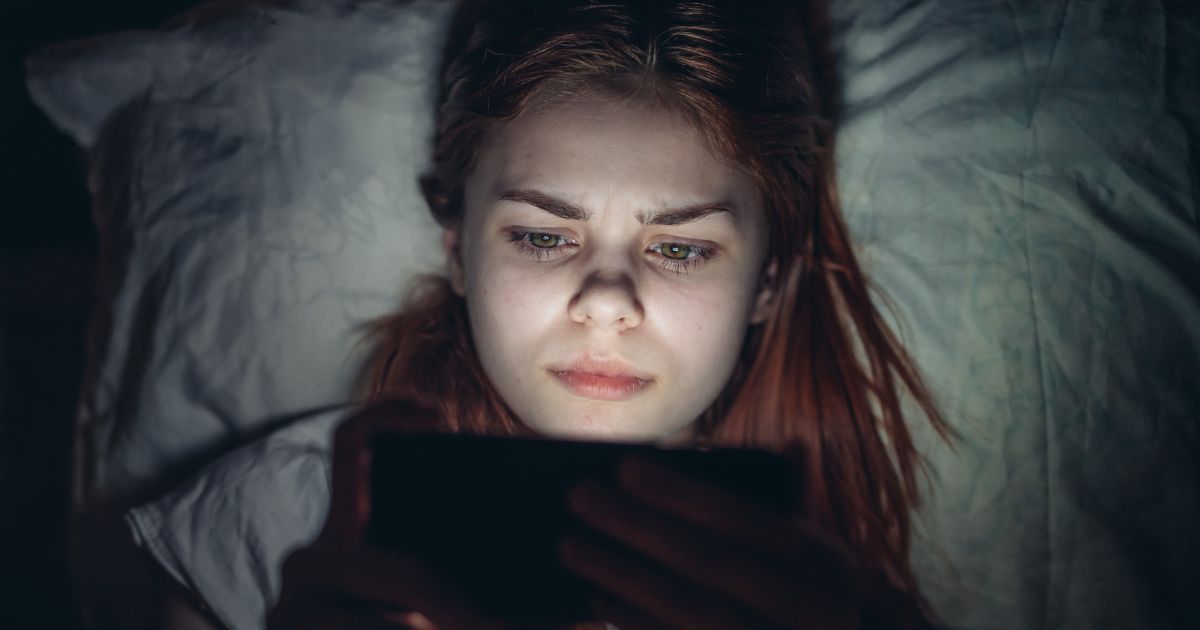 This image shows a young girl lying in bed looking at her phone before going to sleep.